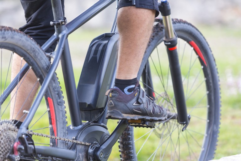 E-cykel Ben og sneakers på pedalerne på en sort e-cykel